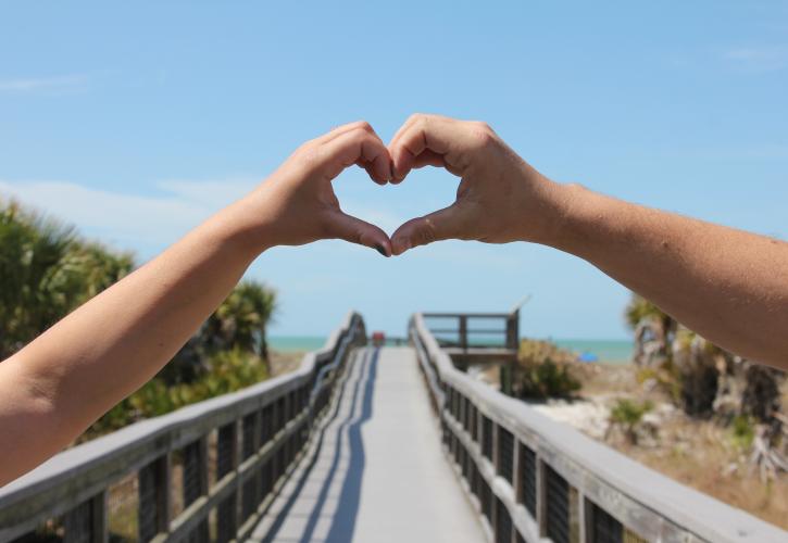 Hand making heart symbol with beach in the background